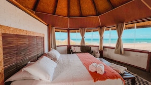 A bedroom with a large bed, a view of the beach, and a wooden ceiling.