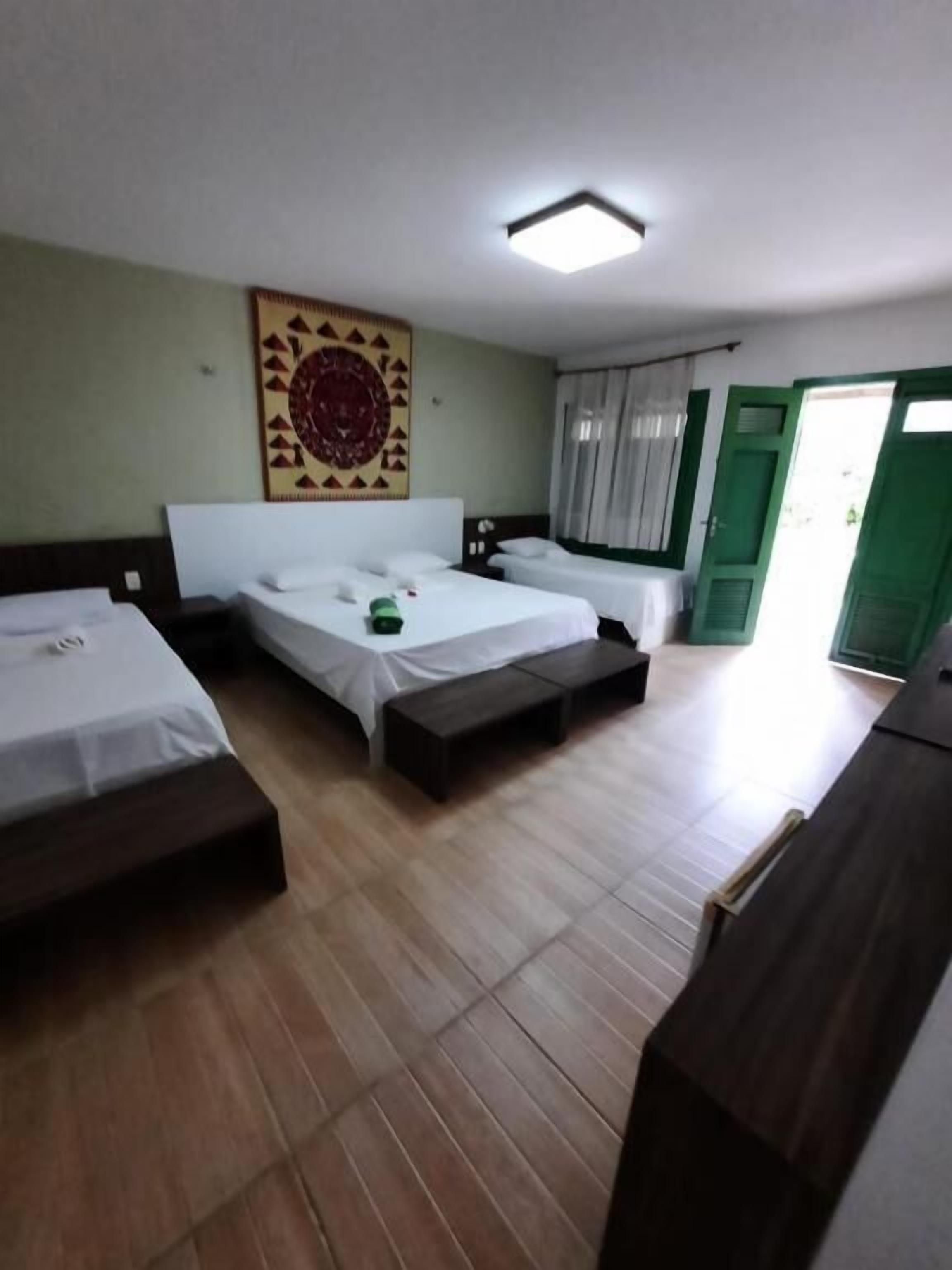 Habitación de hotel con tres camas individuales, un gran tapiz en la pared y una puerta verde.