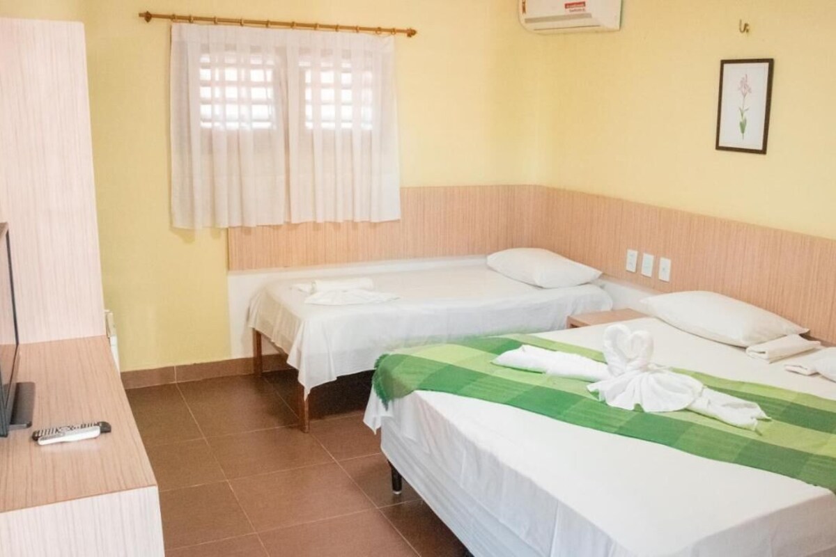 A hotel room with two single beds, a television on a stand, and a window with curtains.