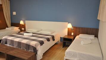 Une chambre d’hôtel avec deux lits simples, un grand lit, une tête de lit en bois, des tables de chevet avec des lampes et un banc.