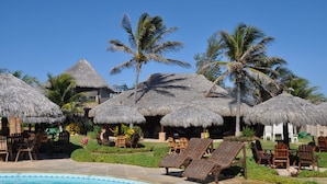 A poolside area with thatched umbrellas, lounge chairs, and palm trees.