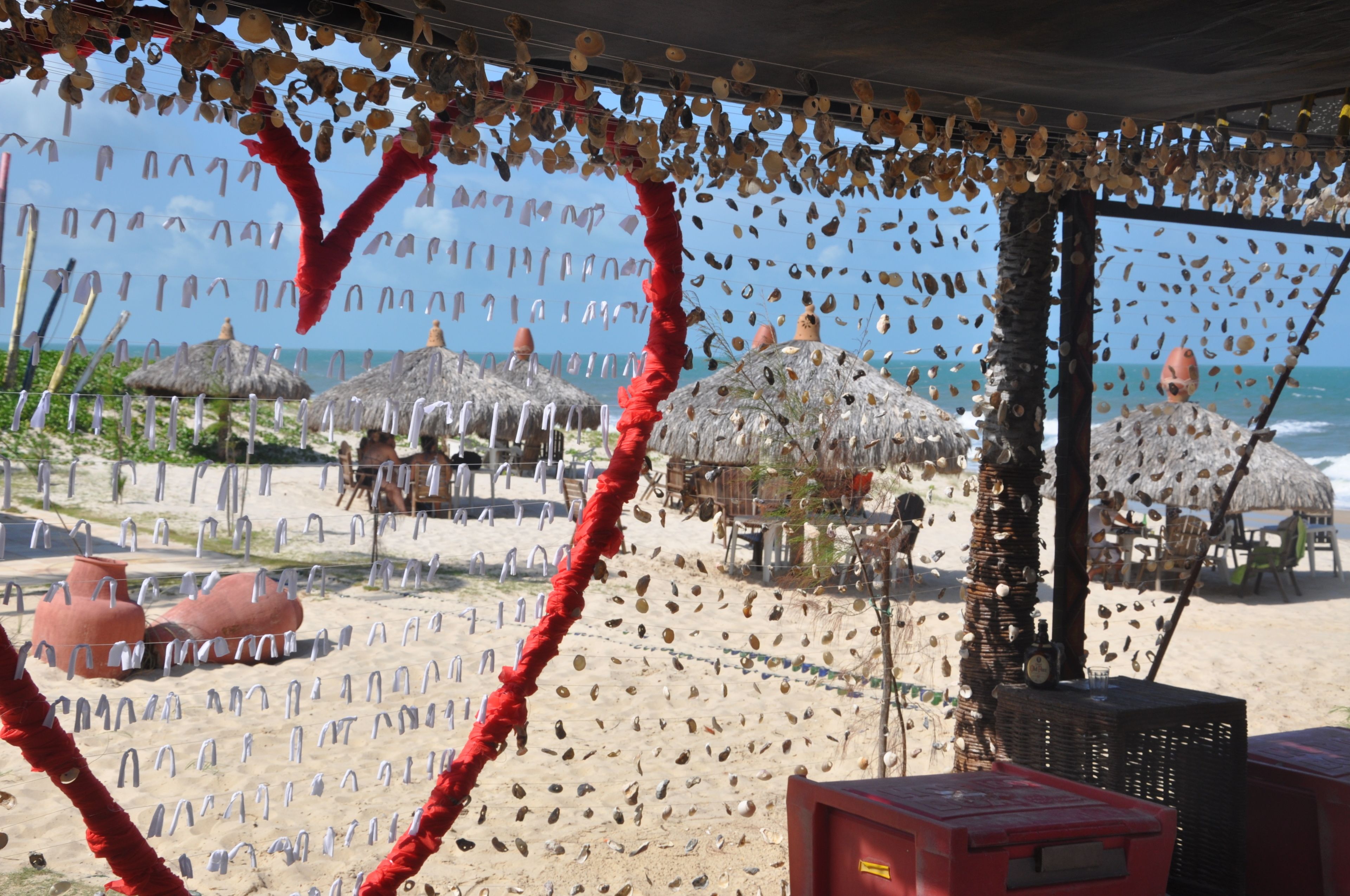 Escena de playa con sombrillas de paja, una barrera de cuerda roja y vista al mar.