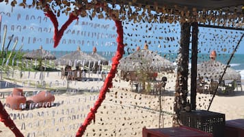 Escena de playa con sombrillas de paja, una barrera de cuerda roja y vista al mar.