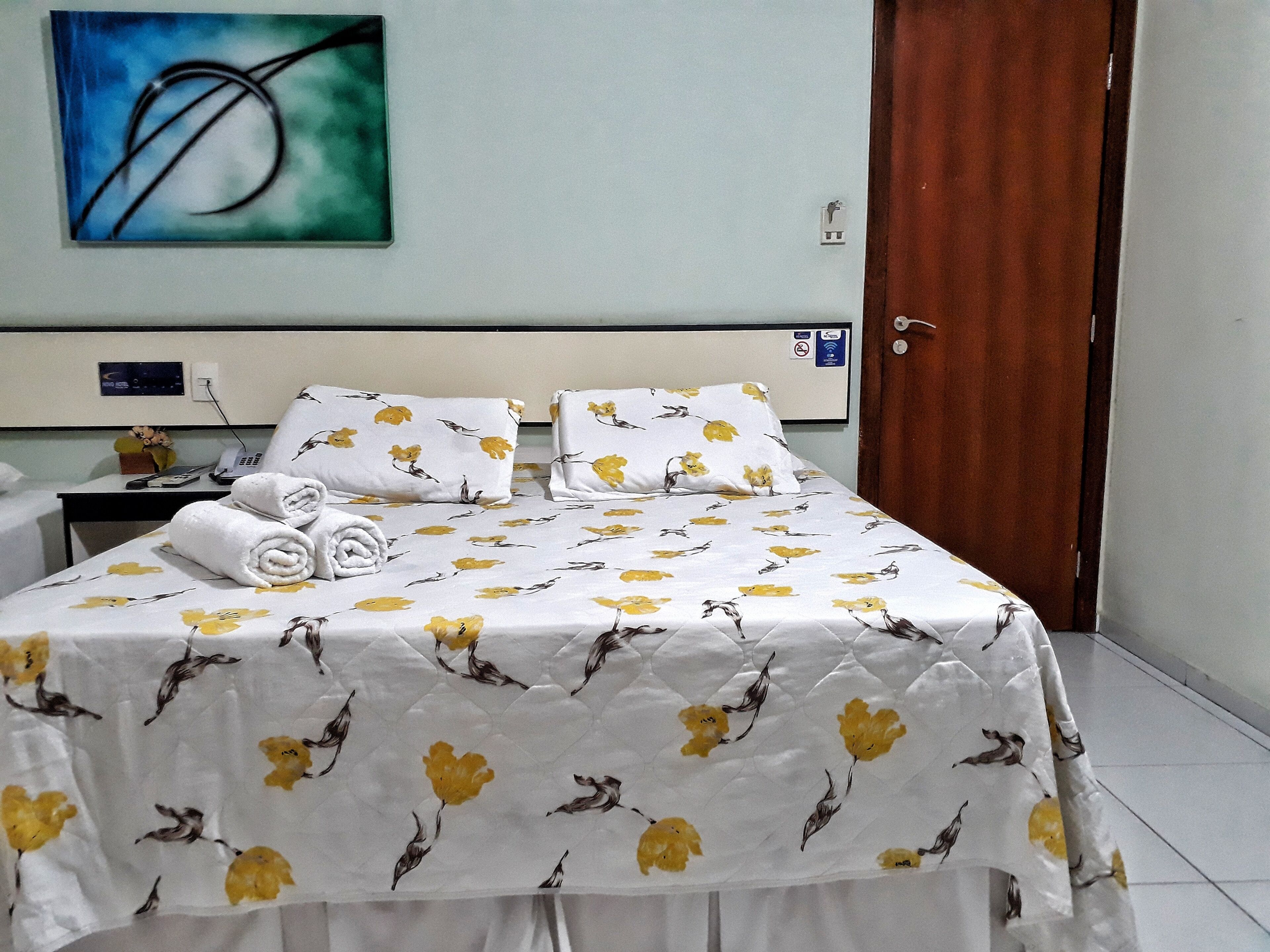 A hotel room with a bed, a nightstand, a telephone, and a painting on the wall.
