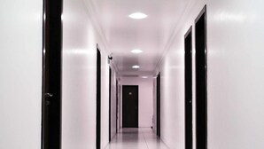 Un long couloir étroit aux murs blancs et aux portes noires, qui mène à une pièce sombre au bout.