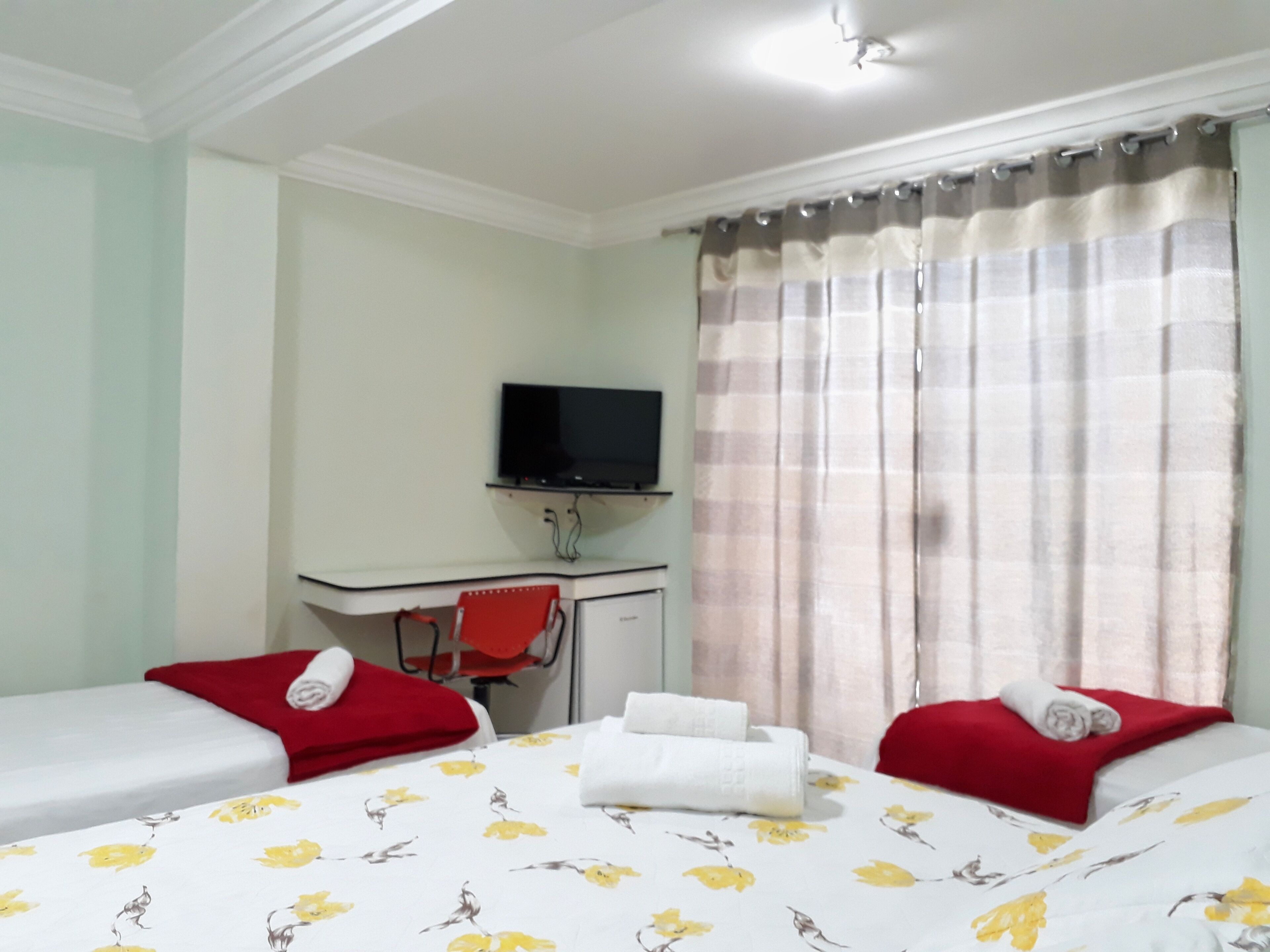 Habitación de hotel con dos camas, un escritorio con televisor y una ventana con cortinas.