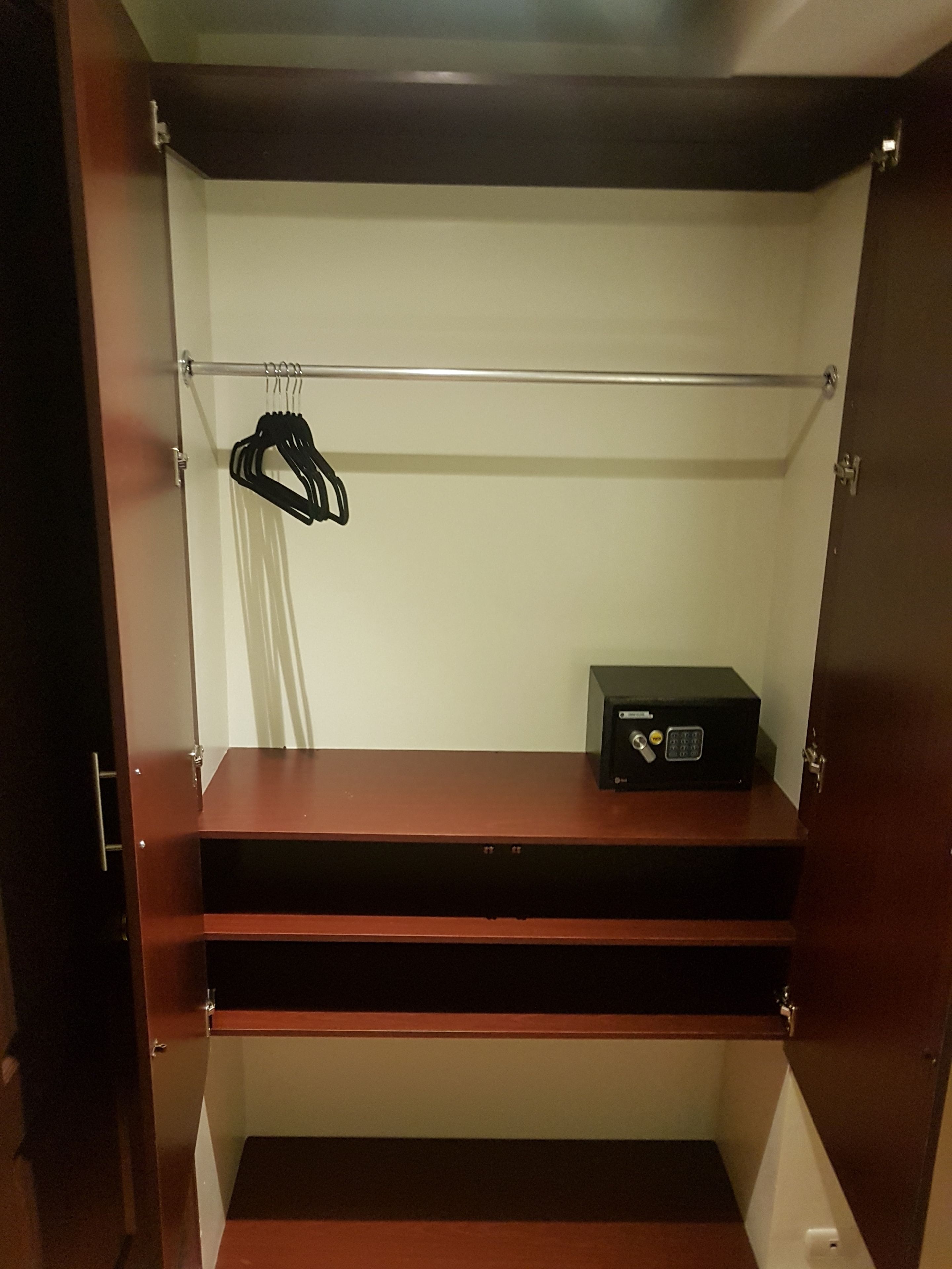 A walk-in closet with a metal rod for hanging clothes, a black safe, and a wooden shelf.