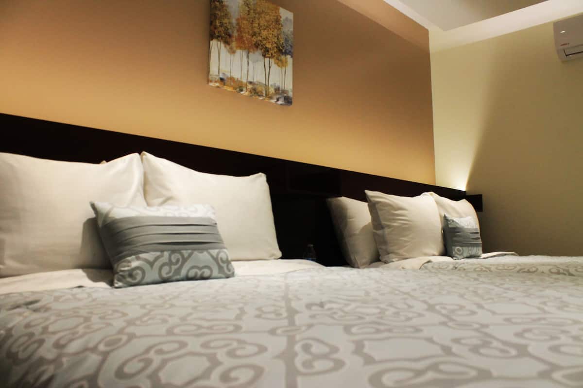 A hotel room with a large bed, multiple pillows, and a painting on the wall.