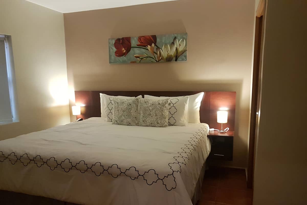 A hotel room with a large bed, two bedside lamps, a floral artwork on the wall, and a nightstand with a phone.