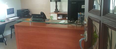En hotellobby med en receptionsdisk i trä, en dator och en skylt med texten ”HOTEL All Day Inn & Suites”.