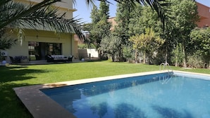 Una piscina con superficie de agua cristalina y azul, rodeada de un césped bien cuidado y varios árboles.