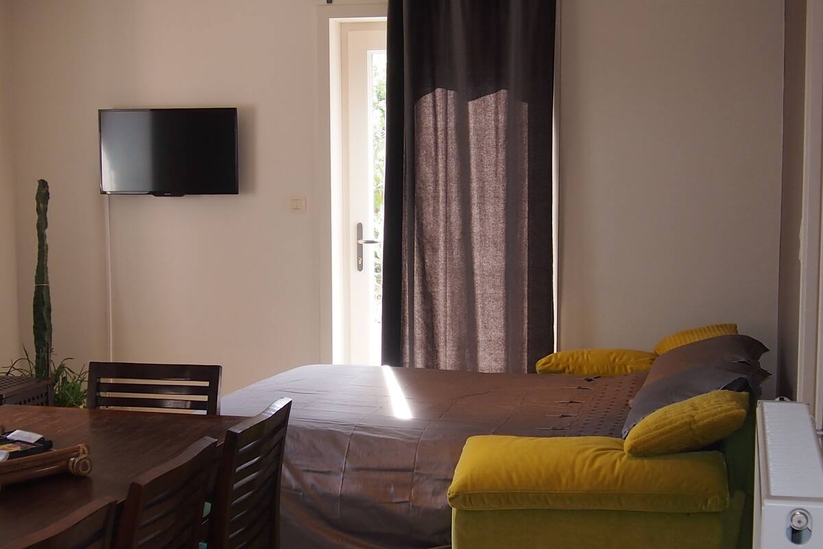 A bedroom with a bed, a desk, a chair, a television, and a window with curtains.