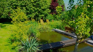 A serene garden with a pond, a wooden bridge, and lush greenery. - Gite L'archipel (Ellezelles)