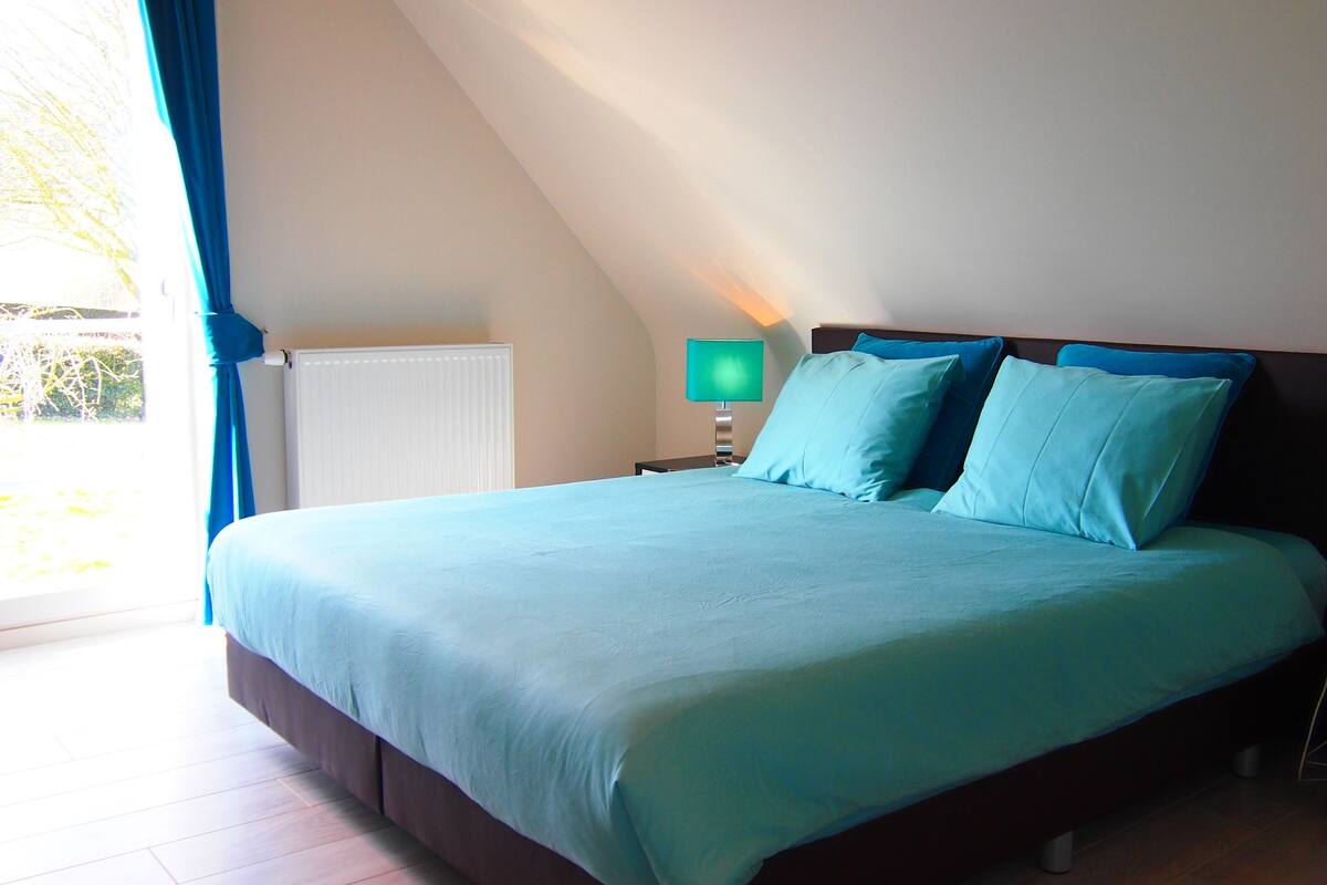 A bedroom with a bed, two bedside tables, a nightstand, a window with curtains, and a radiator.