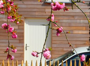 A wooden house with a white door and a car parked in front. - Gite L'archipel (Ellezelles)