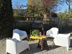 A patio area with white chairs, a small round table, and a grill. - Gite L'archipel (Ellezelles)