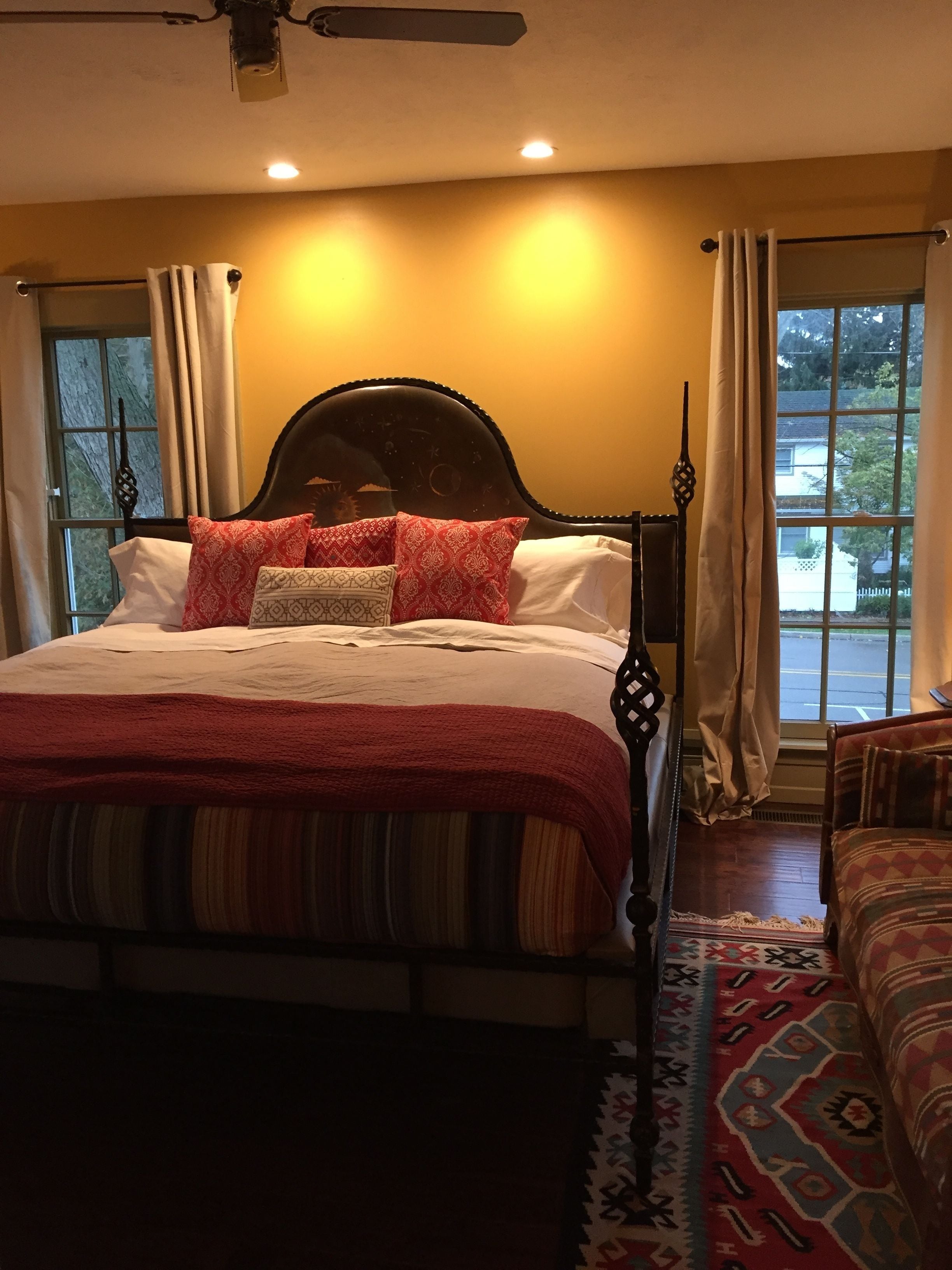 A bedroom with a large bed, a ceiling fan, and a view of the outside through a window.