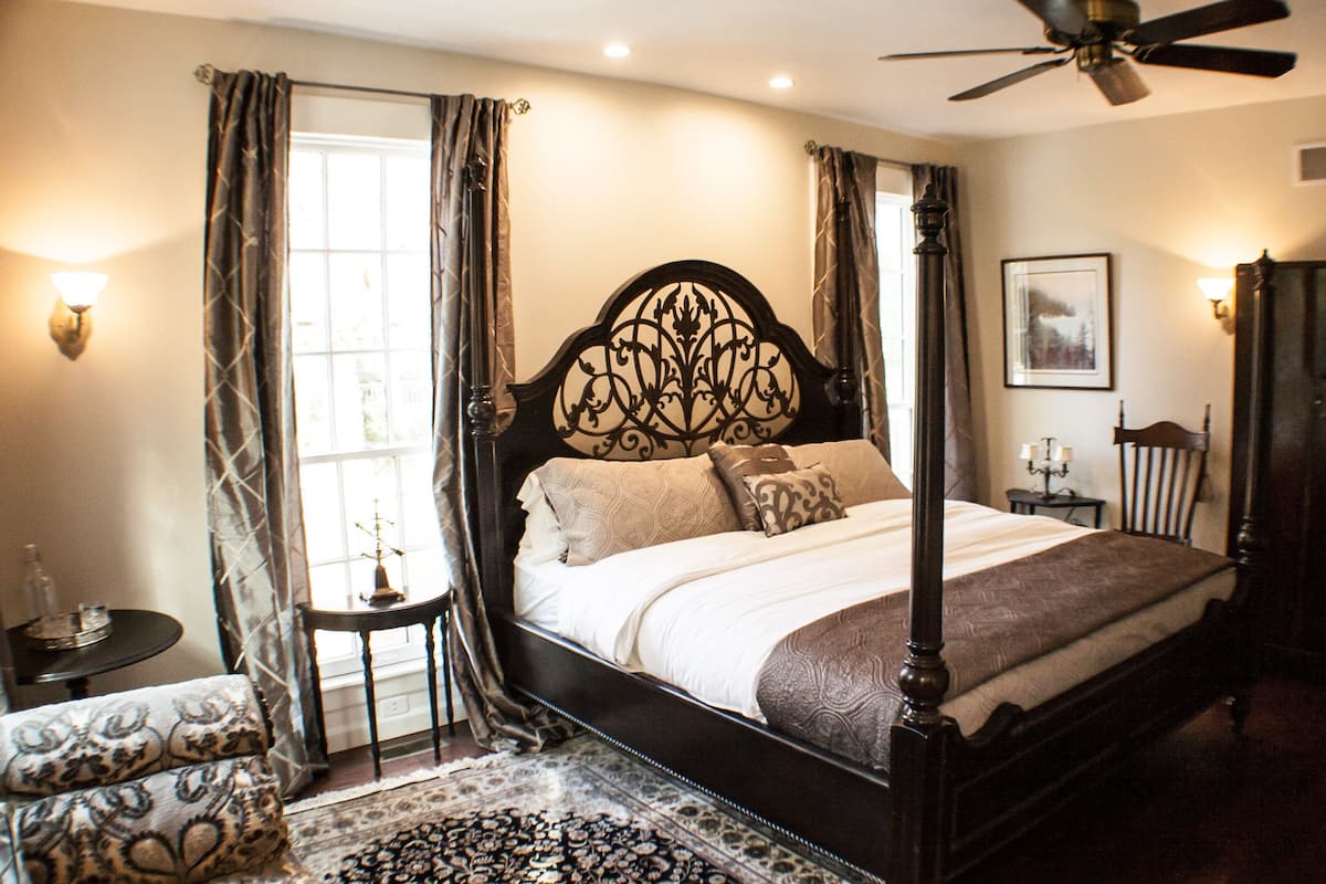 A four-poster bed with a dark wooden headboard, a bedside table with a lamp, and a patterned rug on the floor.