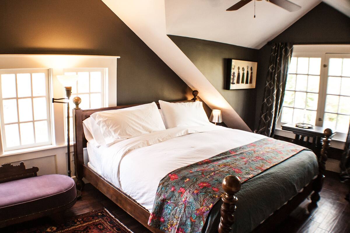A bedroom with a large bed, a wooden bench, a desk, and a ceiling fan.