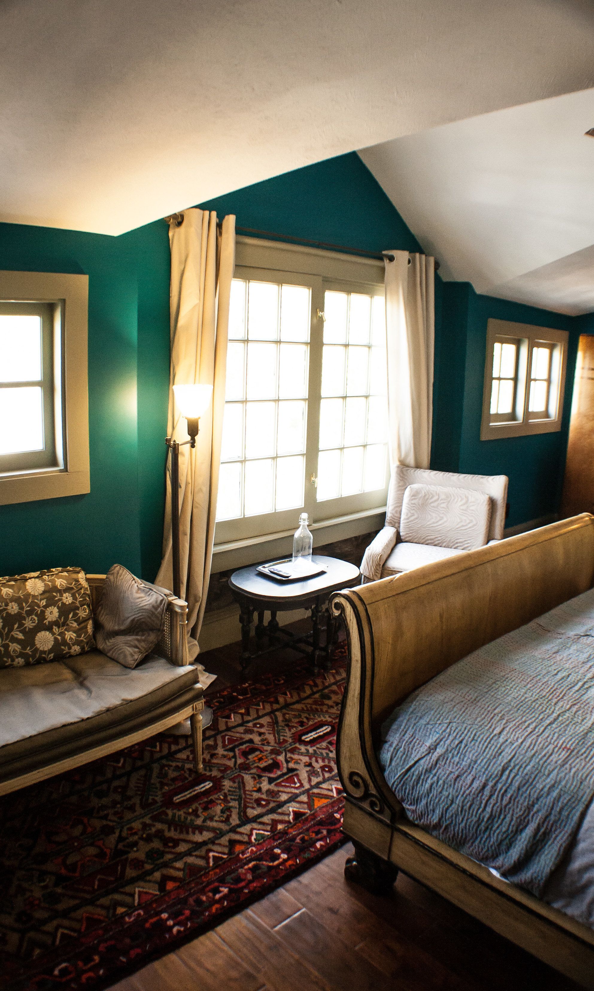 A bedroom with a bed, a chair, a small table, and a window with curtains.