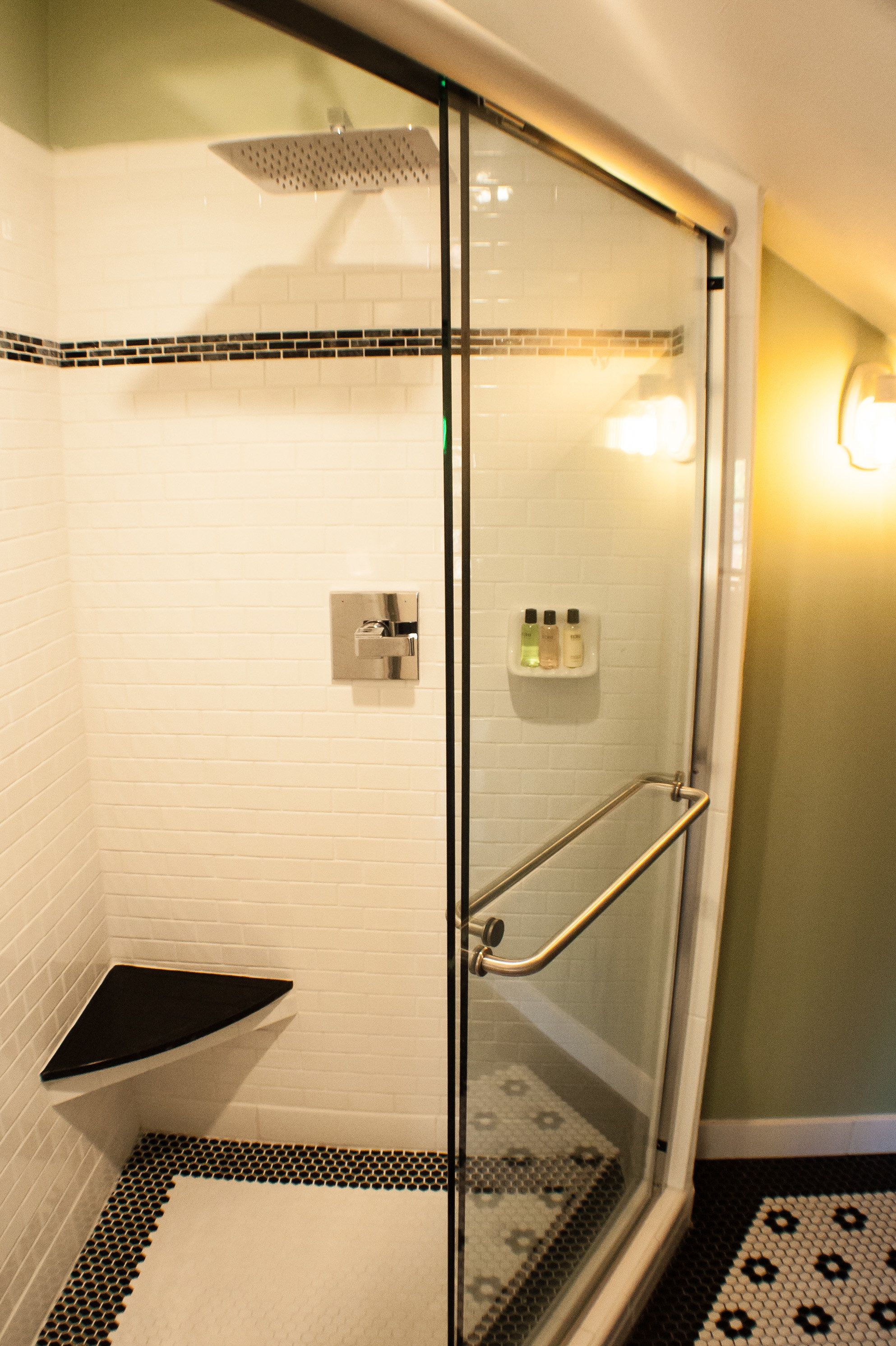 Une douche entièrementClose avec des parois en verre, un siège noir, des murs recouverts de carreaux blancs et un sol à motifs.