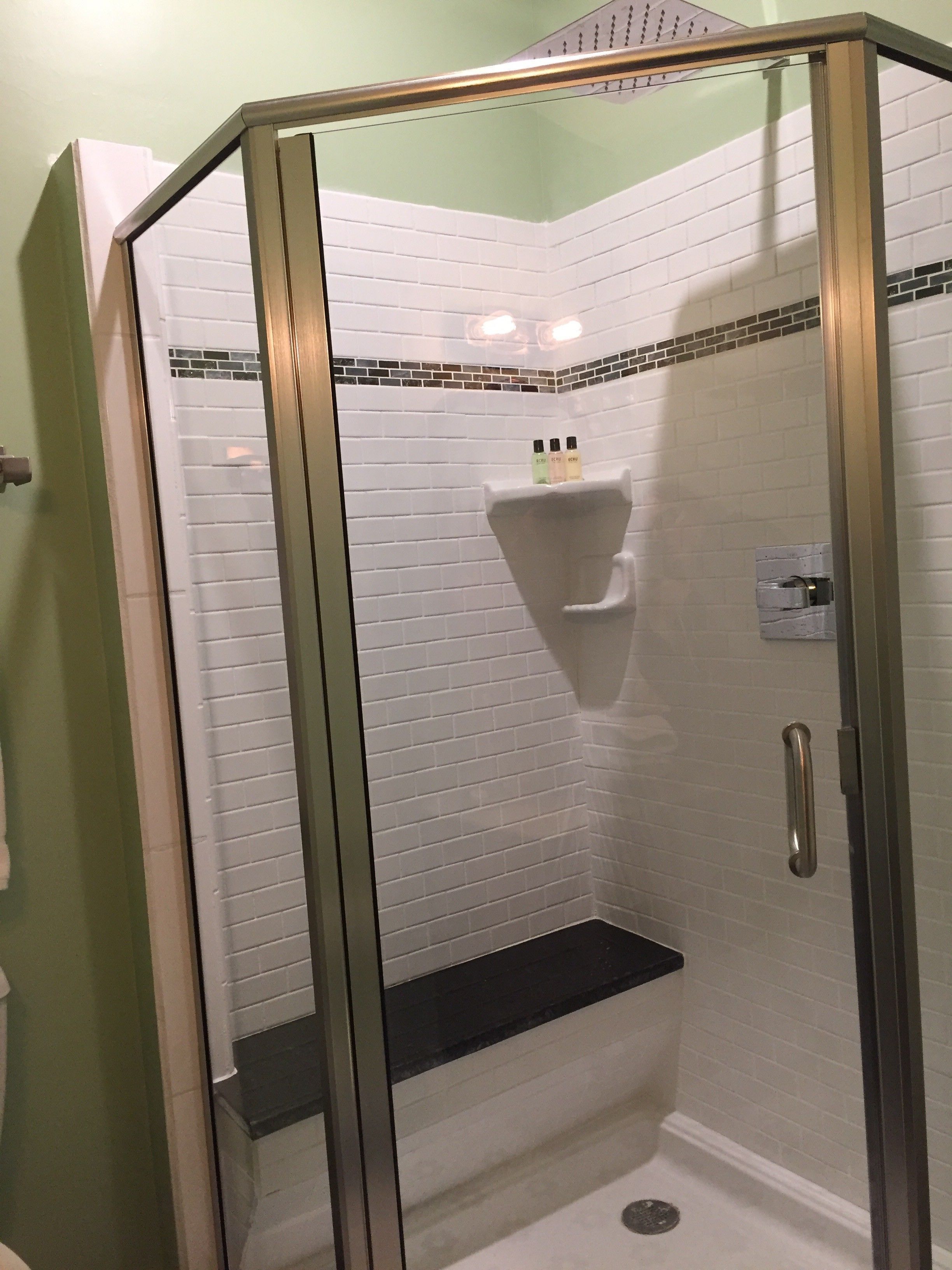 A glass-enclosed shower stall with white subway tiles, a black shelf, and a silver handle.