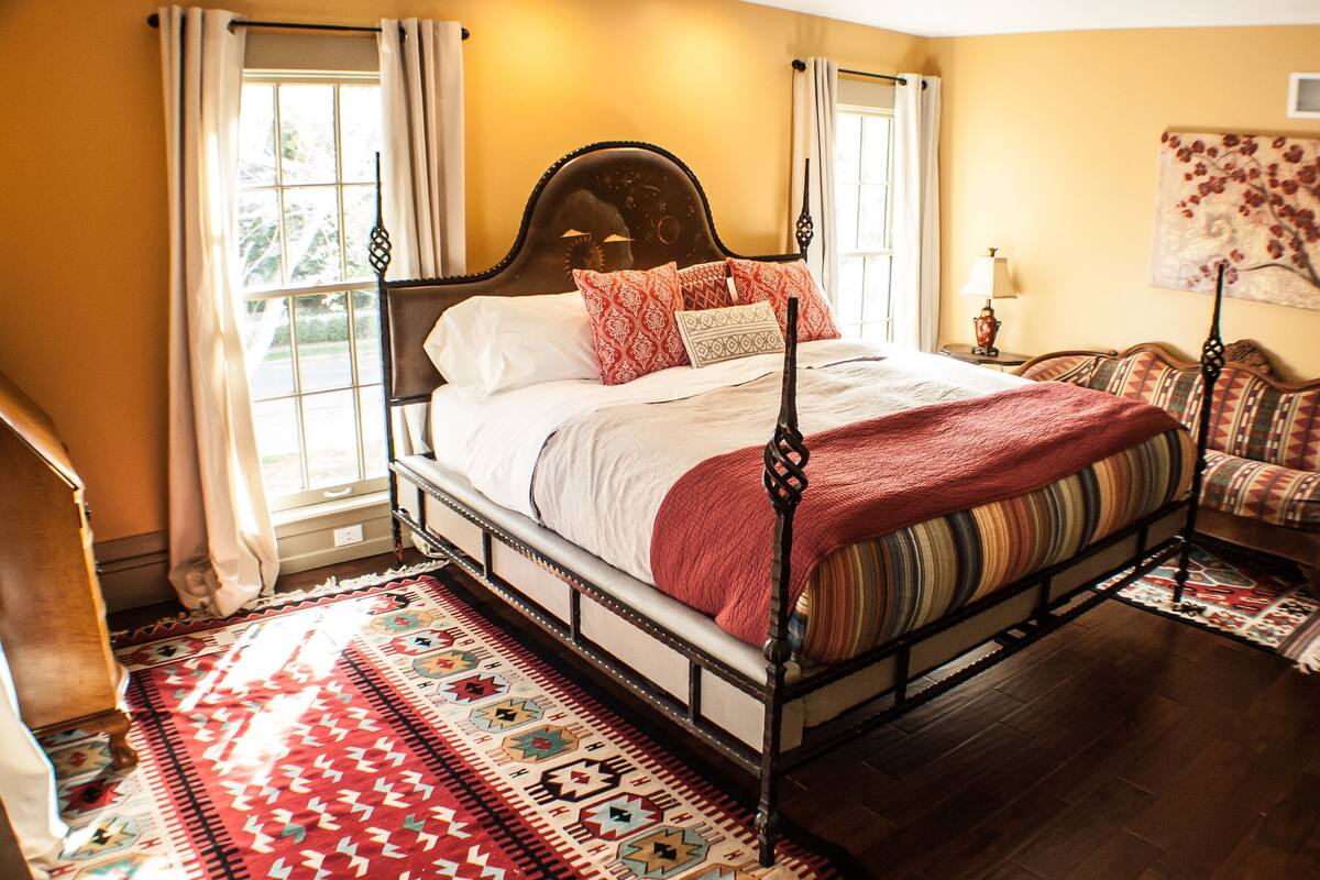 A four-poster bed with a red blanket, a patterned rug, and a sofa with a patterned cushion.