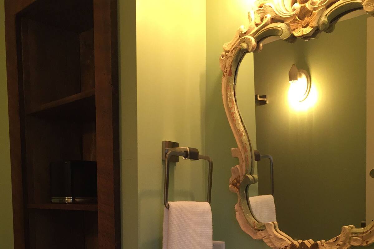 A bathroom with a white sink, a mirror with an ornate frame, a towel hanging on a rack, and a shelf with toiletries.