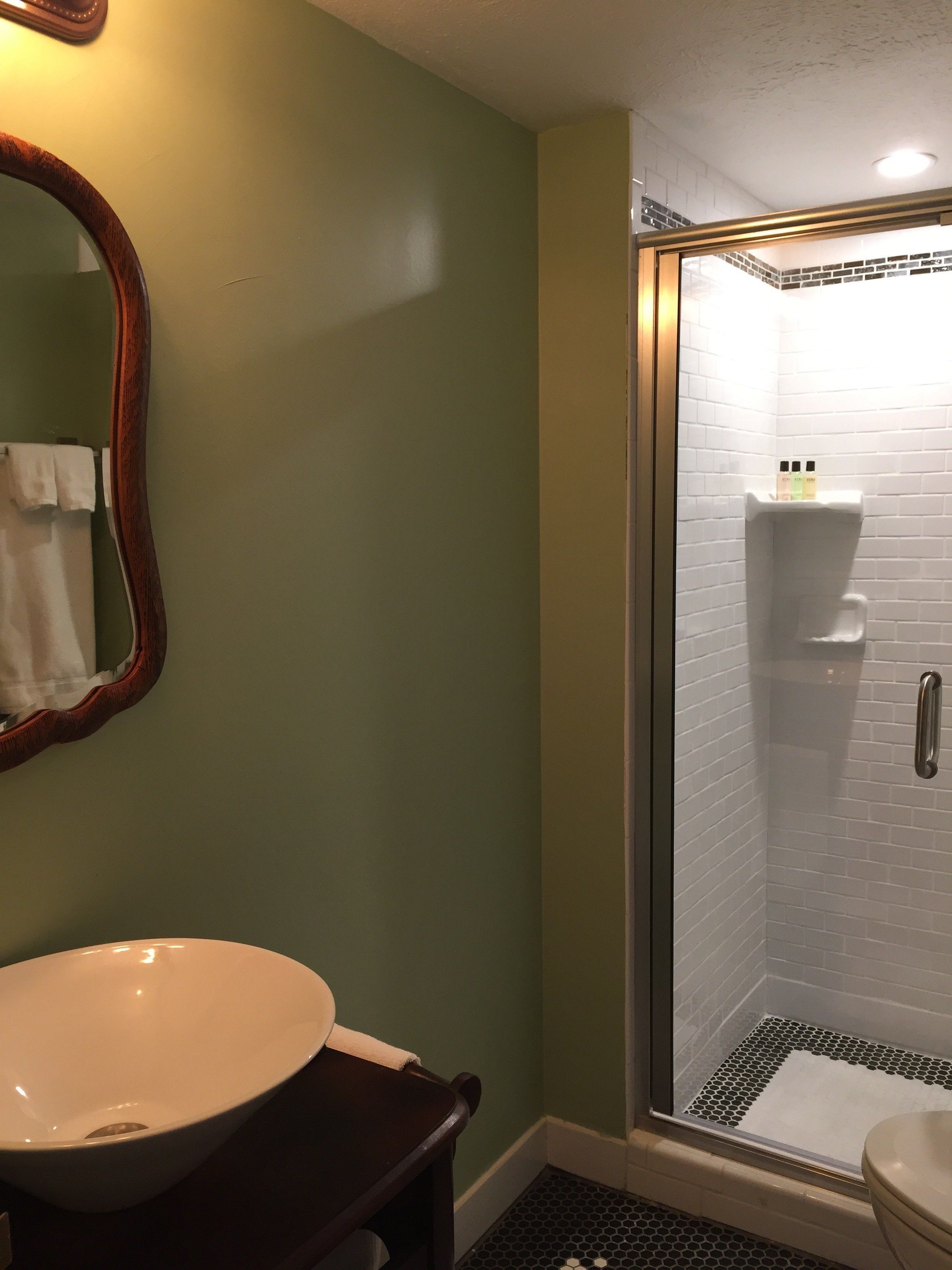 A bathroom with a white sink, a wooden vanity, a mirror, and a glass-enclosed shower area with a tiled floor.