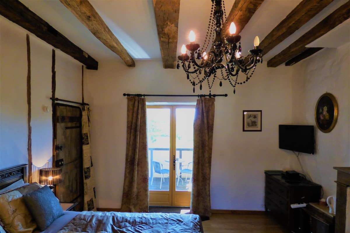 A bedroom with a bed, a chandelier, a wooden wardrobe, a television, and a door leading to an outdoor area.
