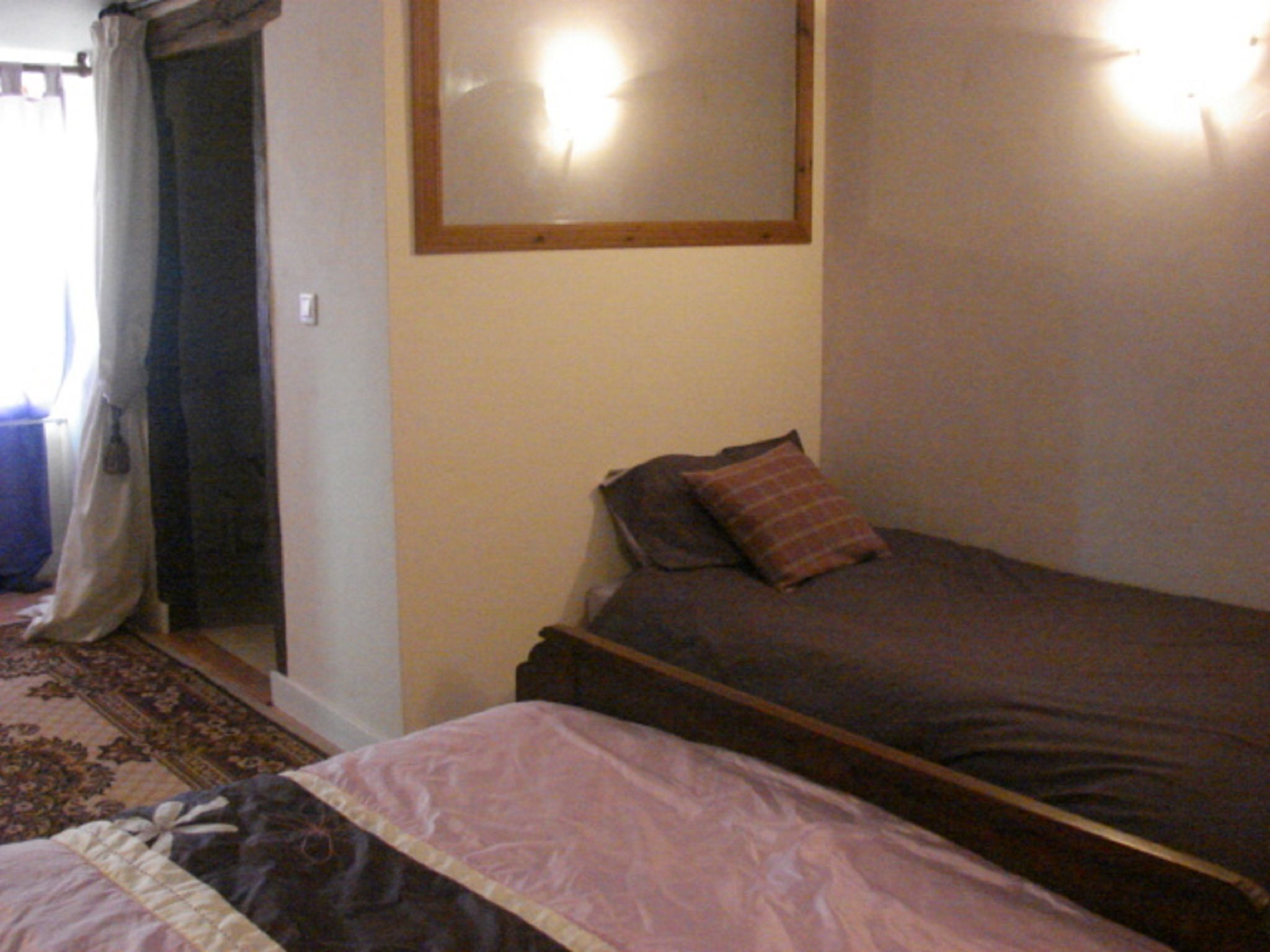 Un dormitorio con una cama, una mesita de noche, un espejo y una ventana con cortinas.