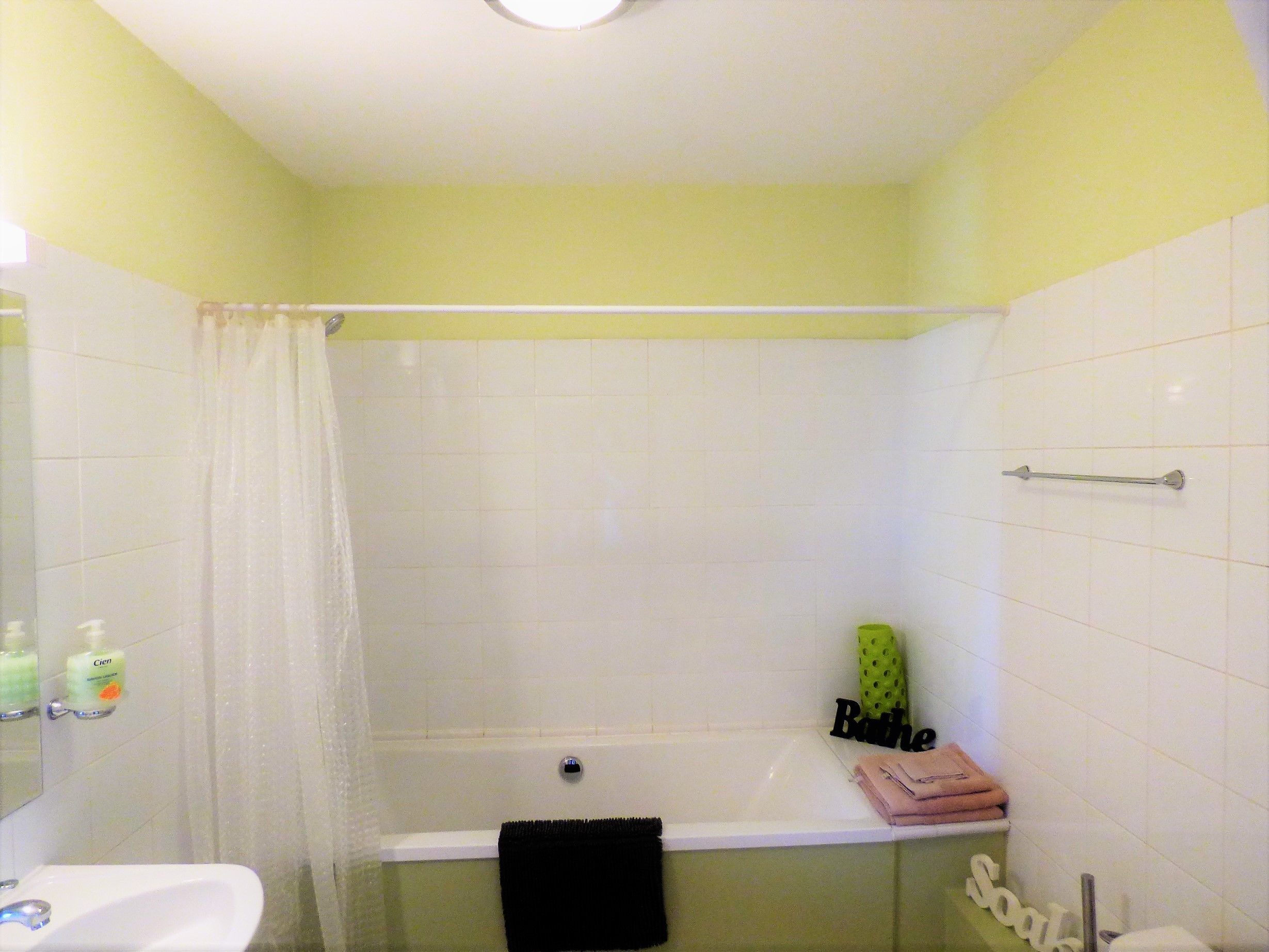 A bathroom with a bathtub, a shower curtain, a sink, and toiletries.