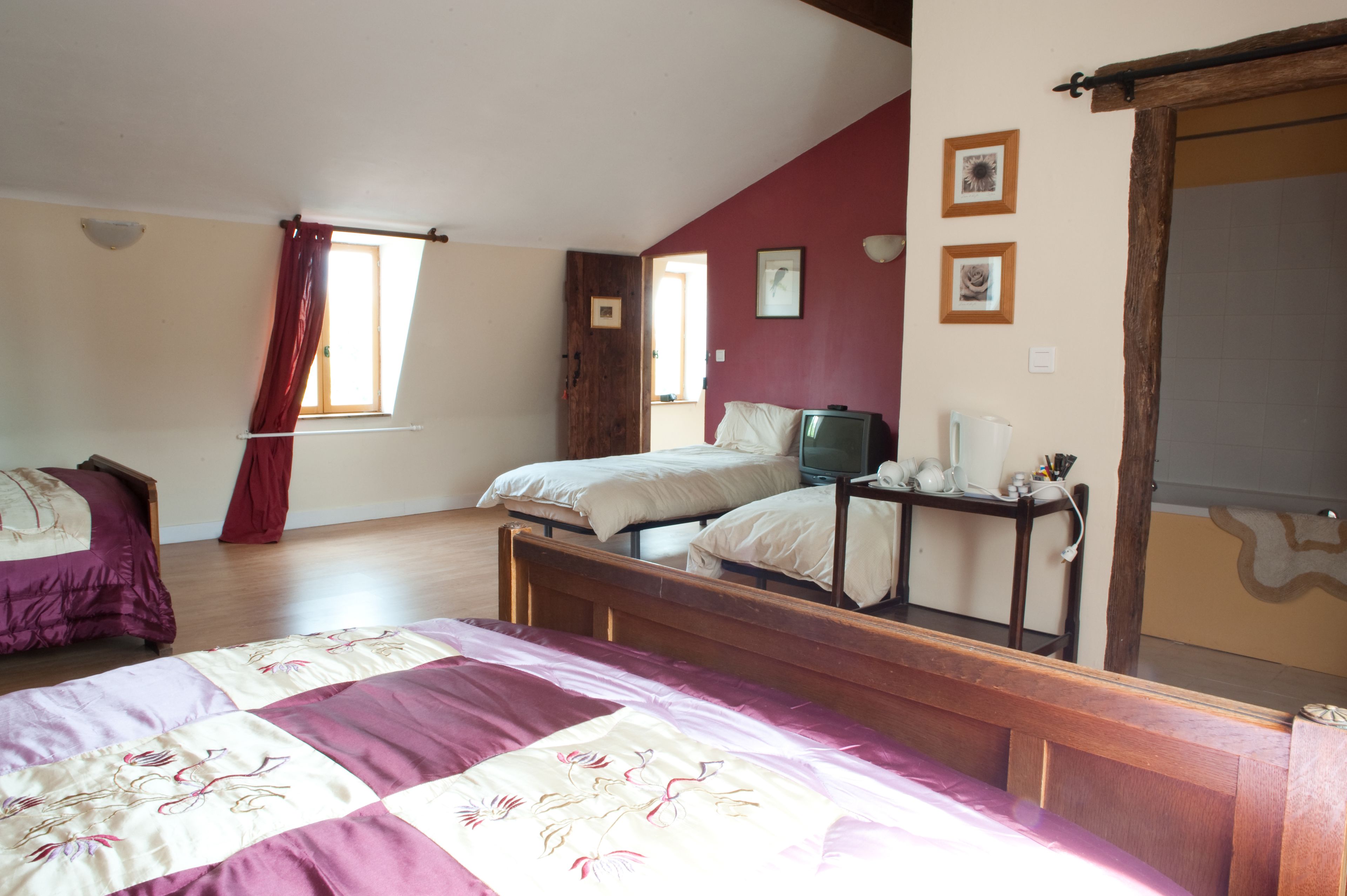 A bedroom with a large bed, two smaller beds, a television, and a bedside table with a lamp.