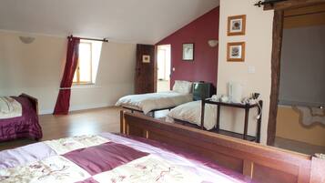 A bedroom with a large bed, two smaller beds, a television, and a bedside table with a lamp.