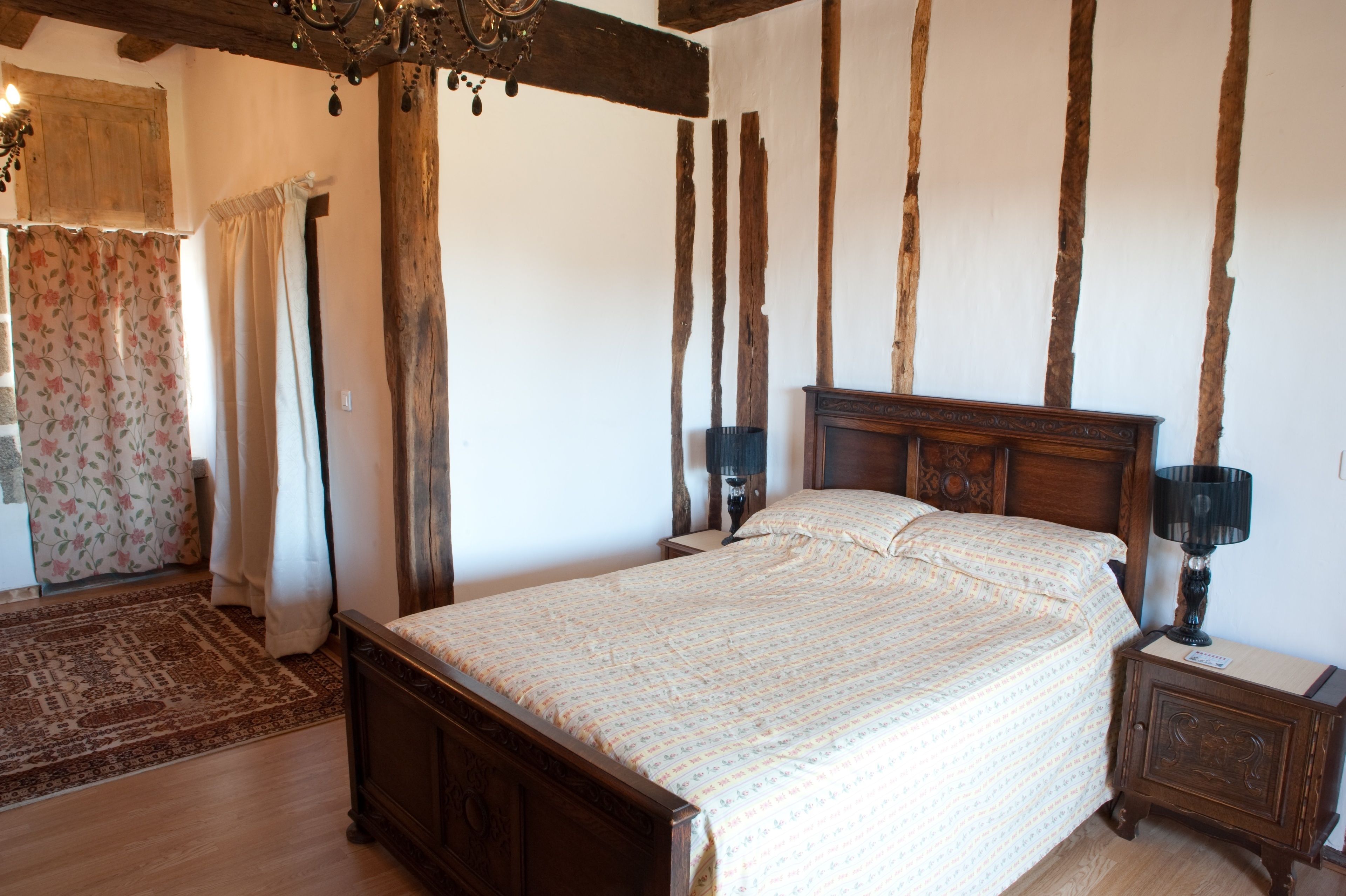 A bedroom with a wooden bed, two bedside tables, a nightstand, a chandelier, and a floral curtain.