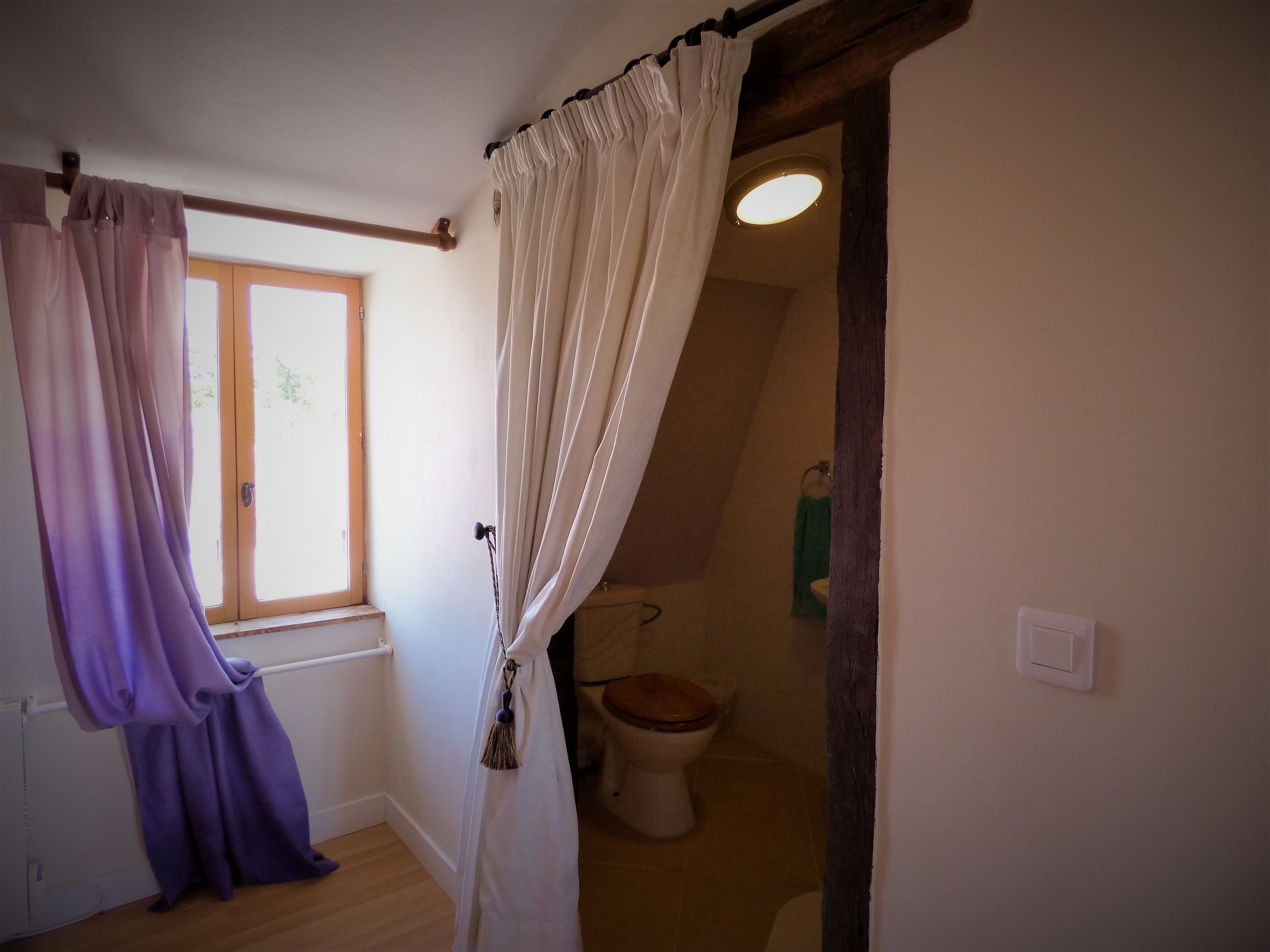 Ein Badezimmer mit Holzboden, einer weißen Toilette und einem Fenster mit Vorhängen.