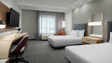A hotel room with a desk, two beds, a TV, and a large window with curtains.