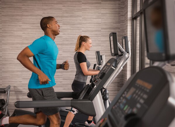 Dos personas corriendo en cintas de correr en un gimnasio con diseño moderno y ventanas amplias.