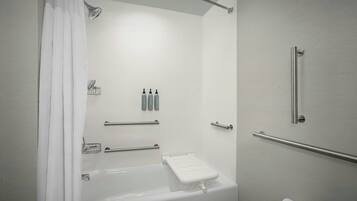 Un baño moderno con bañera, ducha e inodoro. Hay barras de apoyo, un perchero para toallas y un dispensador de papel higiénico.