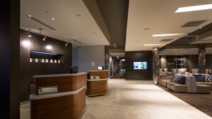 A modern hotel lobby with a reception desk, seating area, and a television screen.