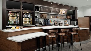 A modern bar area with a white countertop, bar stools, and shelves stocked with bottles and glasses.