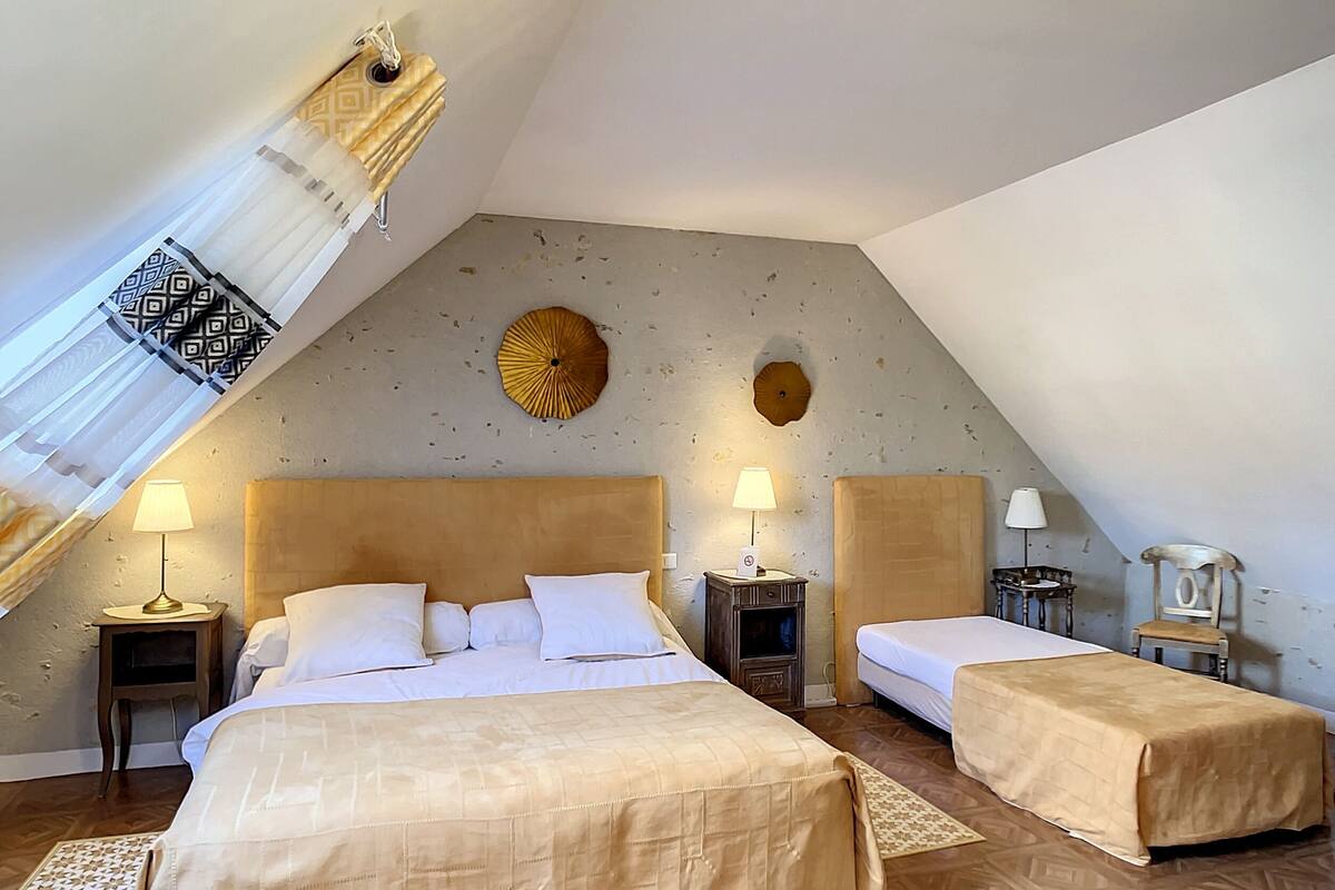 A cozy attic bedroom with two beds, a small table, and a chair.