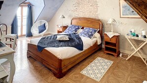 Ein Schlafzimmer mit schrägen Wänden, einem Holzbett, einem Sessel, einem Schreibtisch und einem kleinen Tisch mit einer Lampe.