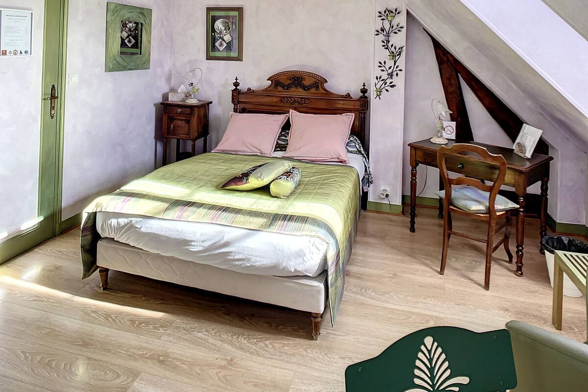 A bedroom with a sloped ceiling, a wooden bed frame, a desk, and a chair.