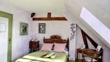 A bedroom with a sloped ceiling, a wooden bed frame, a desk, and a chair.