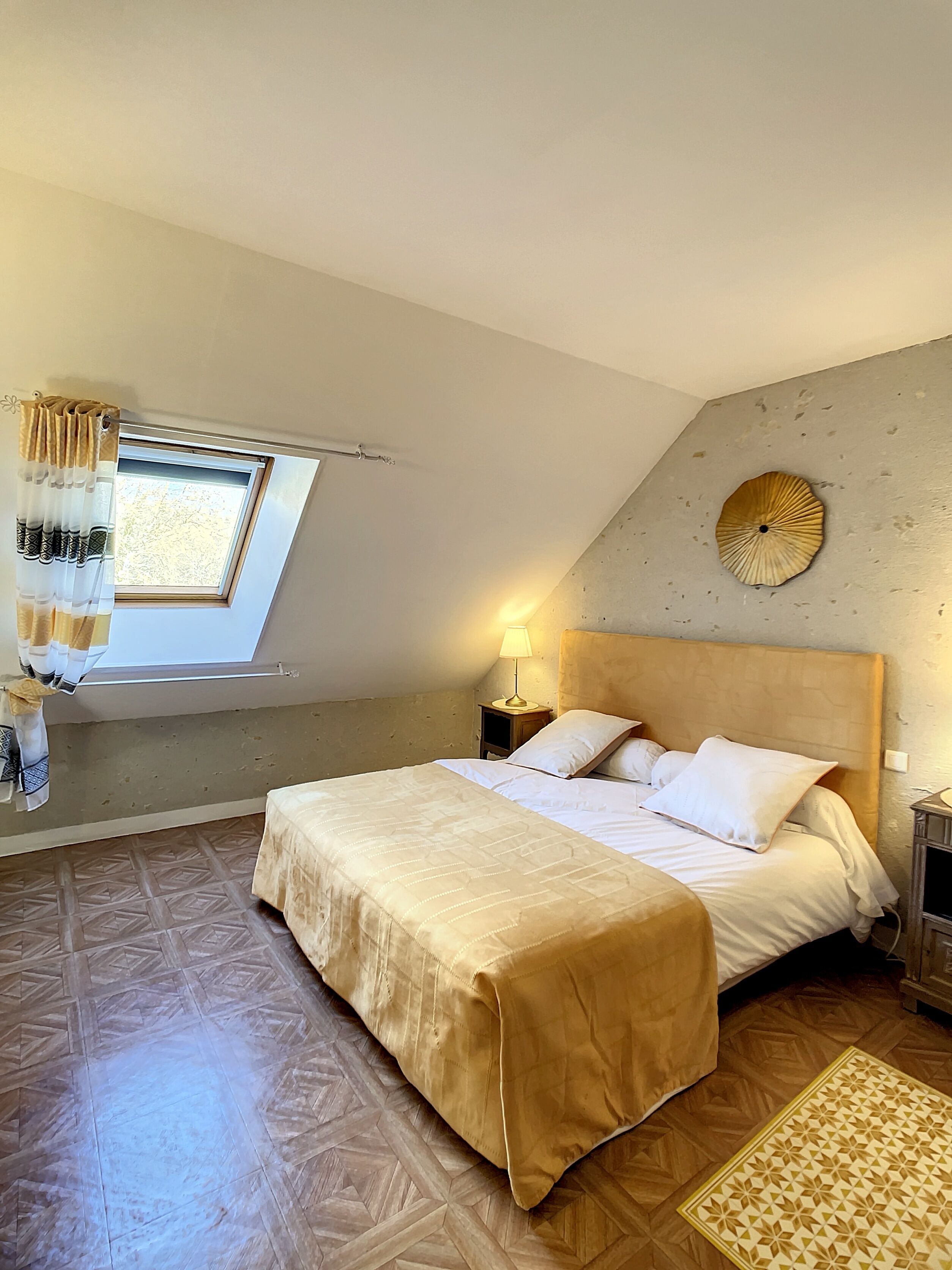 Een slaapkamer met een bed, een raam met gordijnen, een bedlamp, een wandklok en een kamerbreed tapijt met patroon.