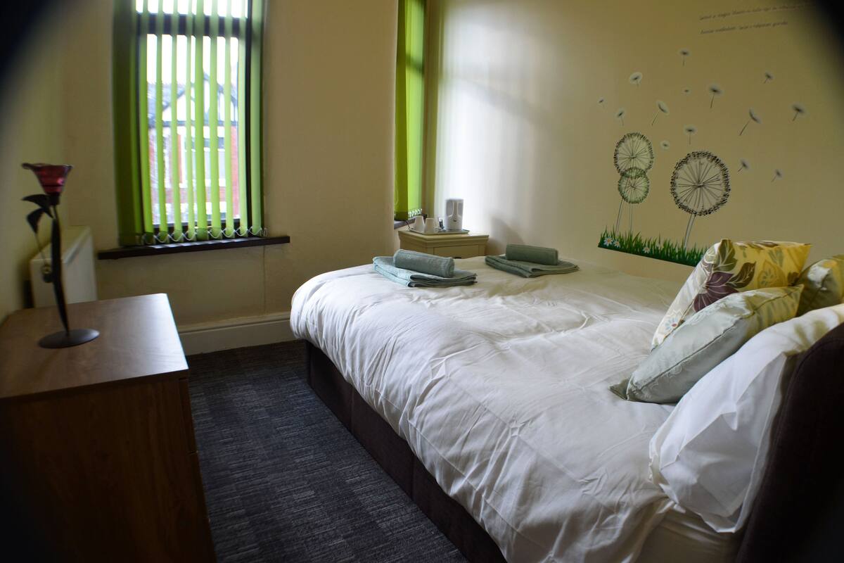 A neatly made bed with pillows and a bedside table with a lamp.