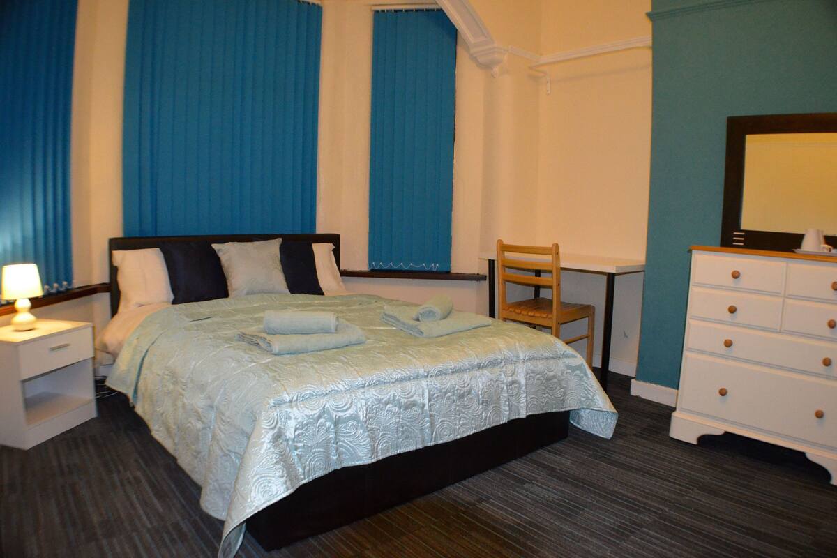 A neatly arranged hotel room with a bed, a desk, a chair, and a dresser.