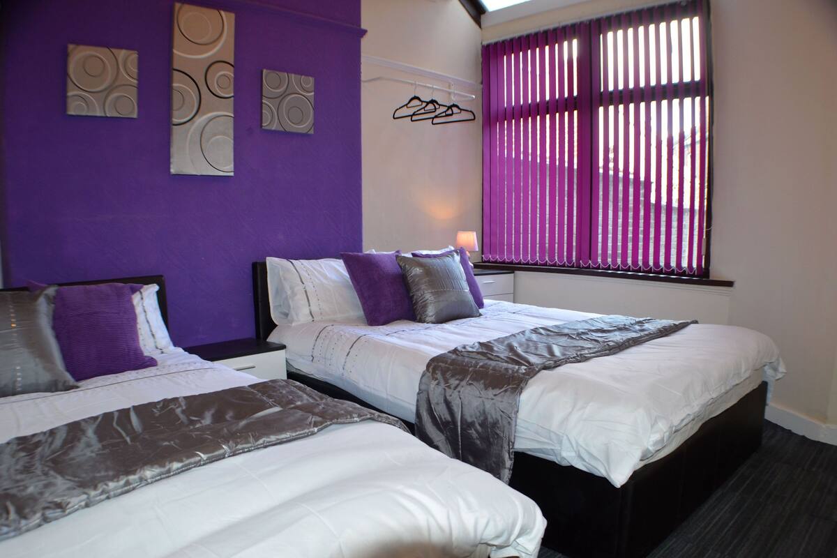 A hotel room with two beds, purple walls, and a window with blinds.