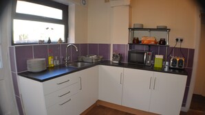 A kitchen with a microwave, toaster, and sink. There are cabinets and a window above the sink. - Birchfields Guest House (Manchester)
